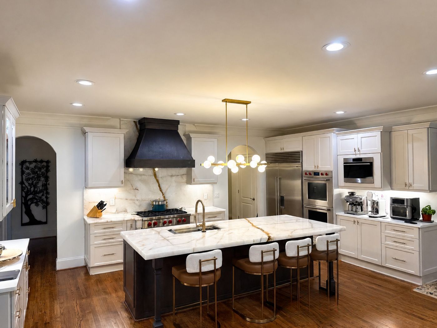 A finished kitchen with white cabinets, a dark hood and a veined stone island